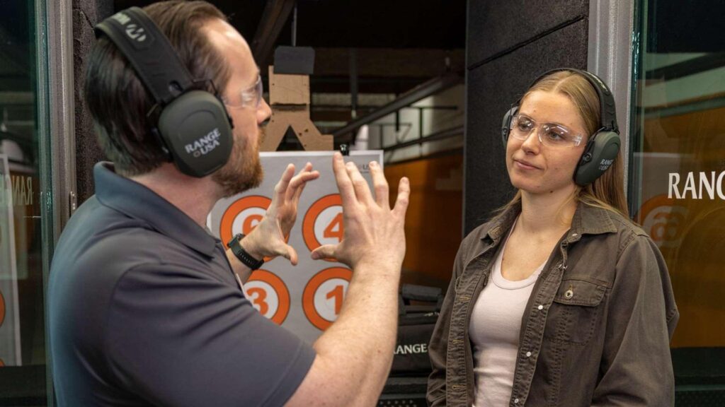 Indoor shooting range visitor discussing eye and ear protection options with a staff member